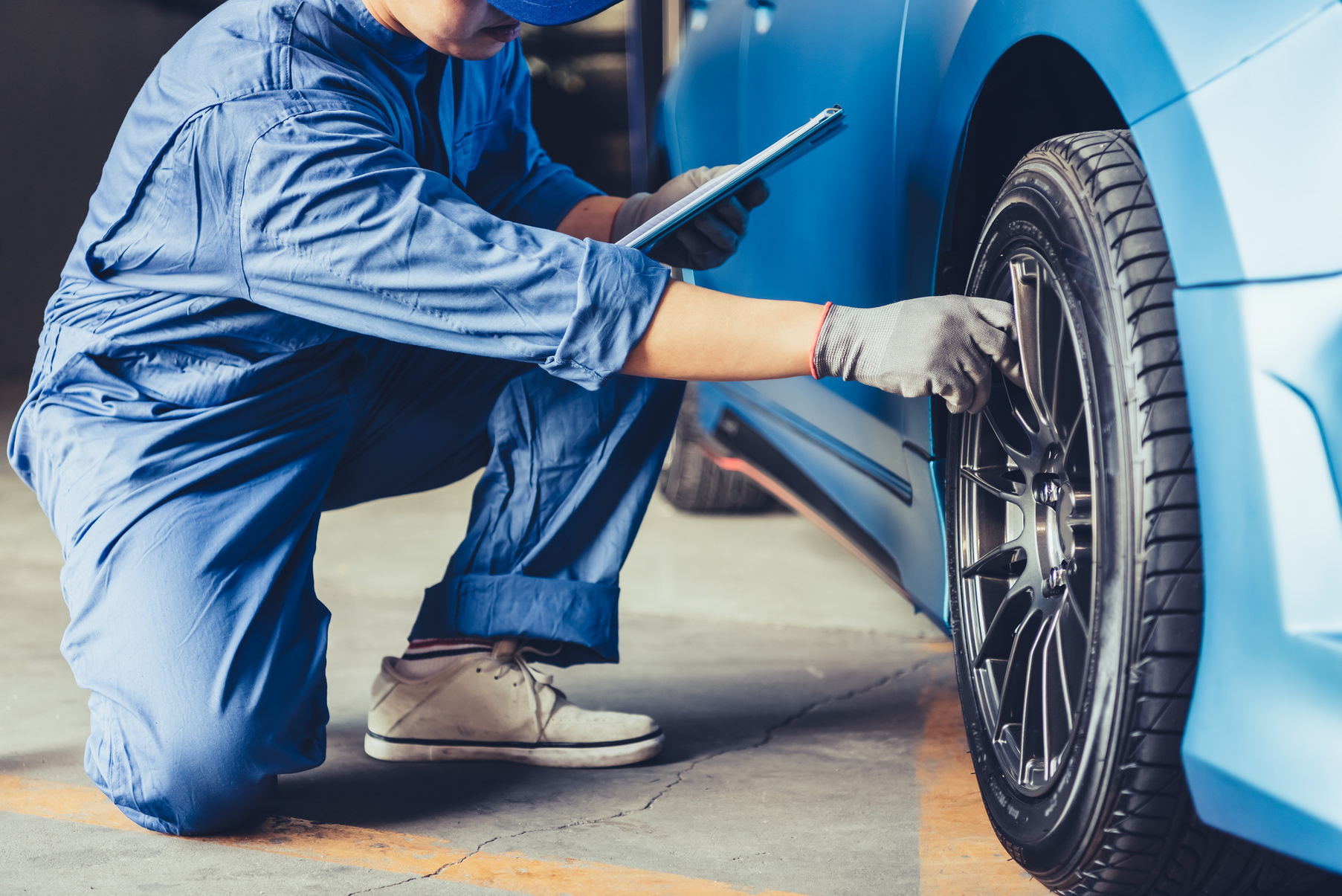 Car Mechanic Holding Clipboard and Checking Tire